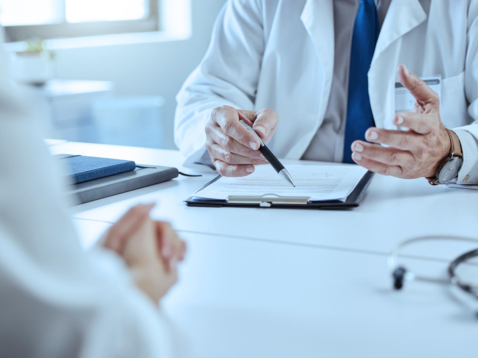 Healthcare professionals discussing documents at a desk, holding a pen and gesturing.