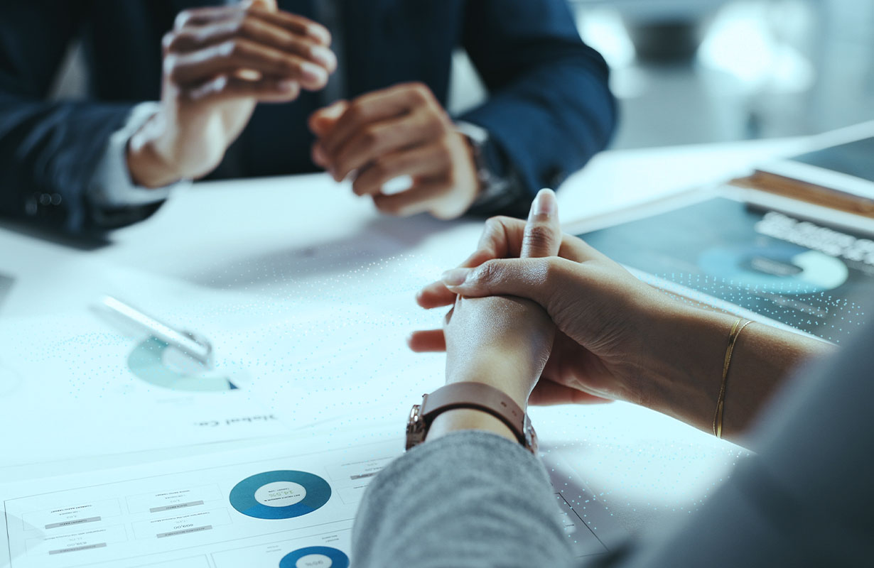 People in an office setting talking with documents visible on the table.