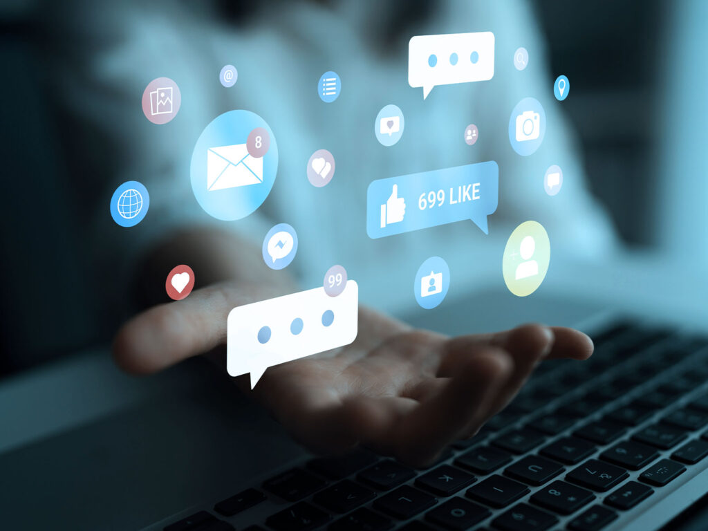 Hand holding floating social media icons and notifications above a laptop keyboard.