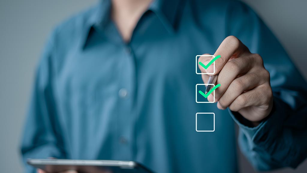 A person in a teal shirt checks two glowing boxes on a transparent digital checklist, with a tablet in hand, conveying productivity and task completion.