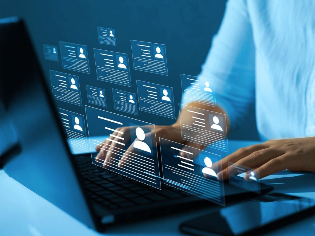 Hands type on a laptop as glowing digital profile cards float above the keyboard, suggesting online networking, data management, and a sleek, futuristic workplace.