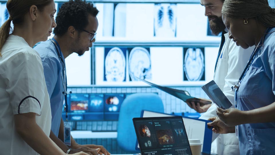 A diverse medical team of doctors and nurses reviews patient scans, X-rays, and computer diagnostics together in a modern hospital control room.